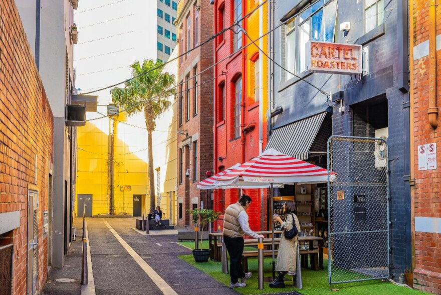 Two people are standing in front of a laneway cafe