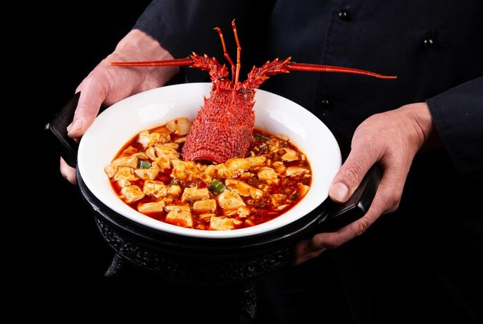 Person serving a Chinese dish with a lobster head sticking out of the bowl.