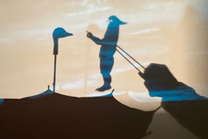 Puppet shadows with upside-down umbrella with duck head handle facing figure, with puppeteer hands visible.