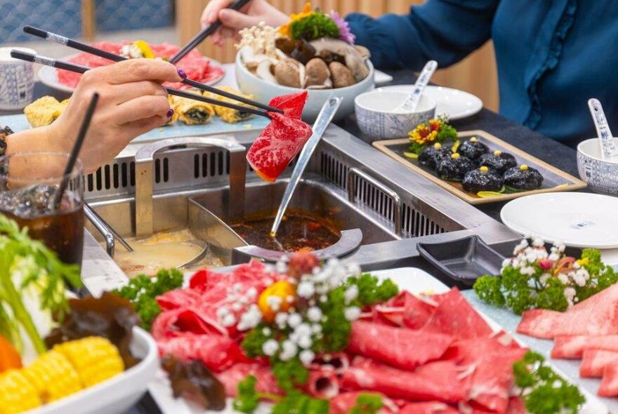 A person's hand lifting a piece of meat into a hotpot tray