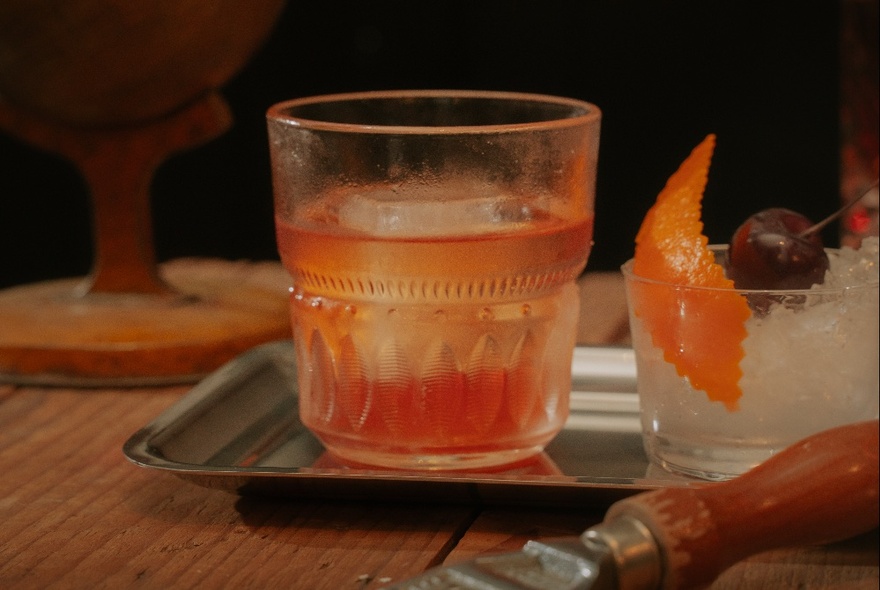 An orange coloured cocktail in a short tumbler on a silver tray.