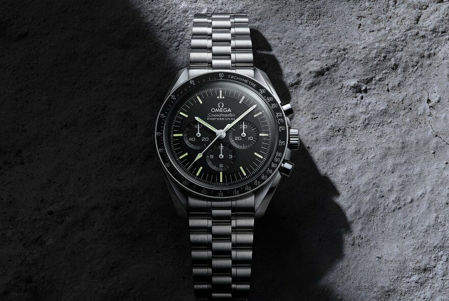 A black Omega watch with a metallic band against a black rock background. 