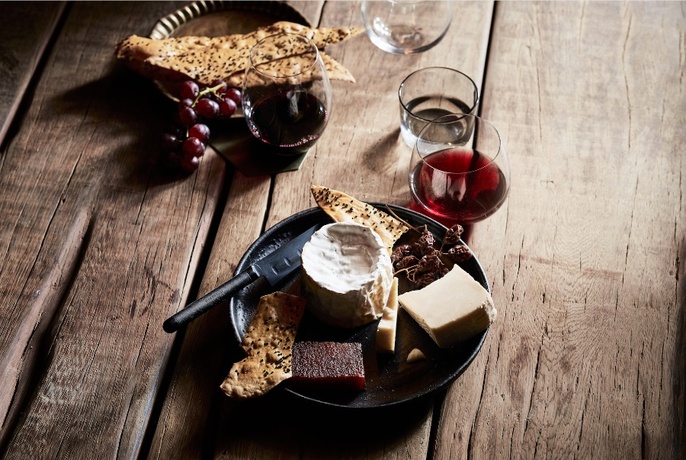 A cheese plate and red wine on a timber table 