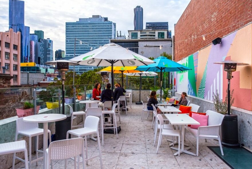 A colourful rooftop bar with a pastel mural overlooking the city skyline. 
