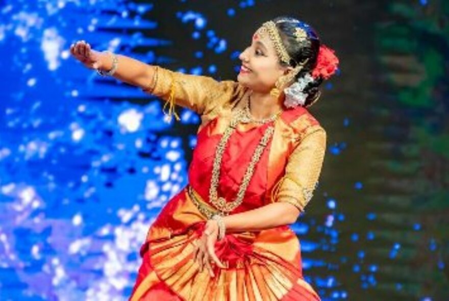 Woman dancing on stage in bright orange and red national costume.