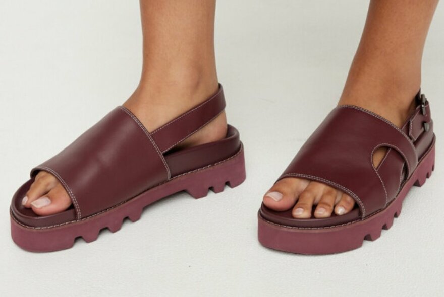 A model wearing chunky burgundy sandals with straps at the back.