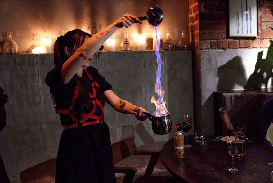 A bartender making a cocktail by pouring a stream of fire into a goblet.