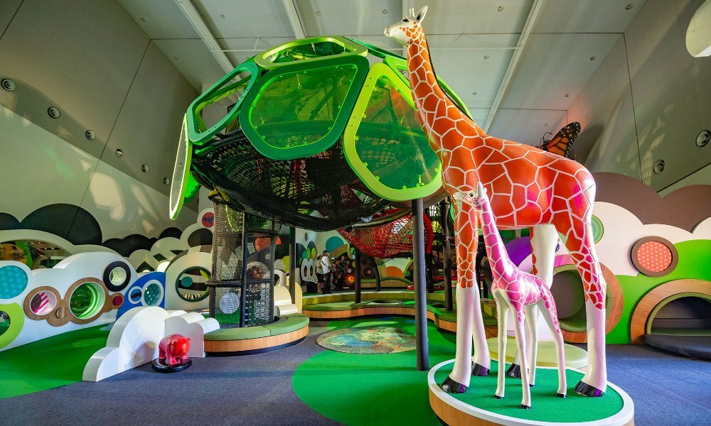 A statue of a mother and baby giraffe in an indoor children's playground.