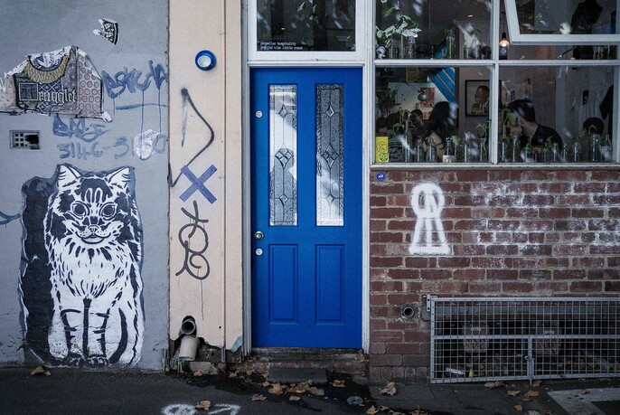 Blue door with cat graffiti to the left and brick wall and windows to the right.