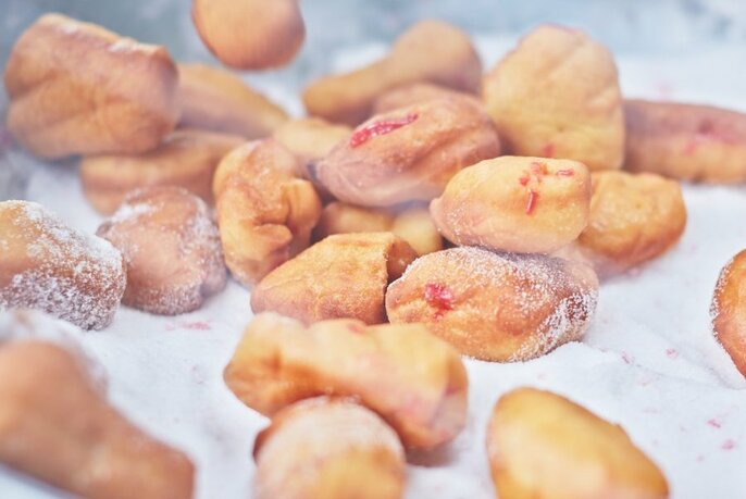 Piles of small, pastry-like jam filled donuts on bed of iced-sugar.