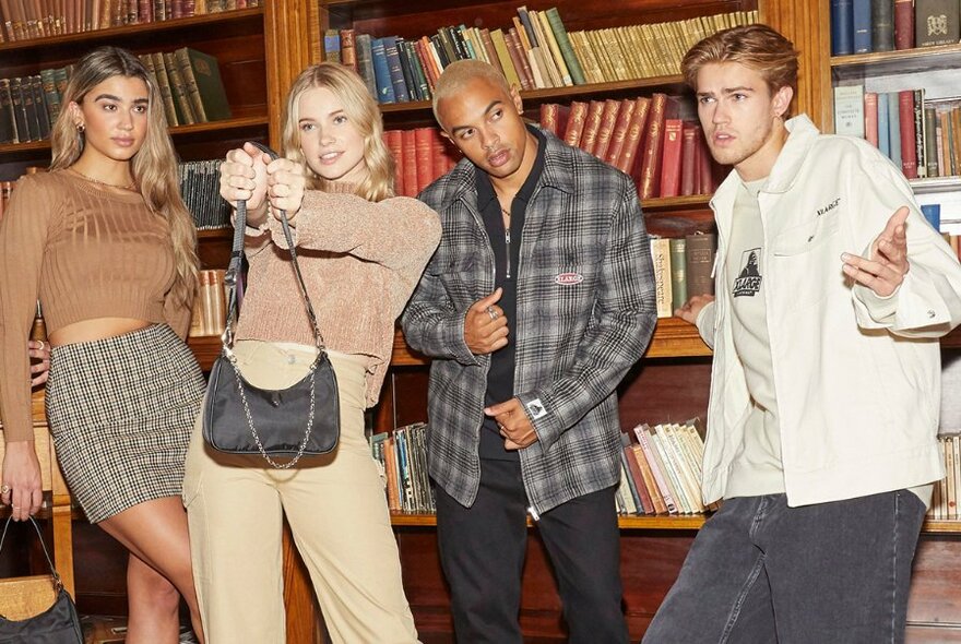 Four models giving sassy poses in neutral toned outfits, in a library.