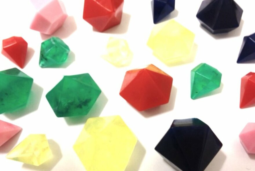 A collection of different coloured small soaps shaped like cut gemstones against a white background.