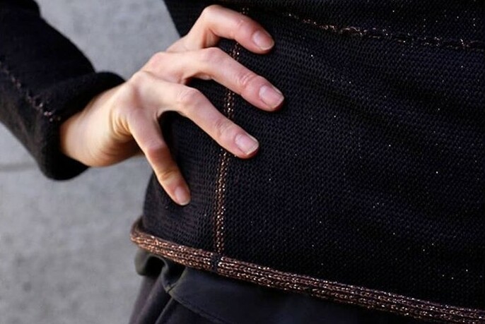 Close up of hand on waist of model wearing dark brown knitted jumper.