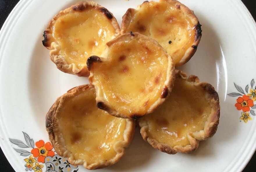 Five Portuguese tarts on a floral plate.