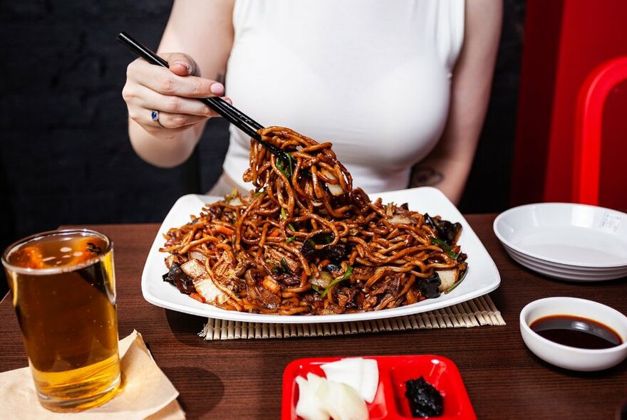 A diner in a restaurant lifting noodles with chopsticks. 