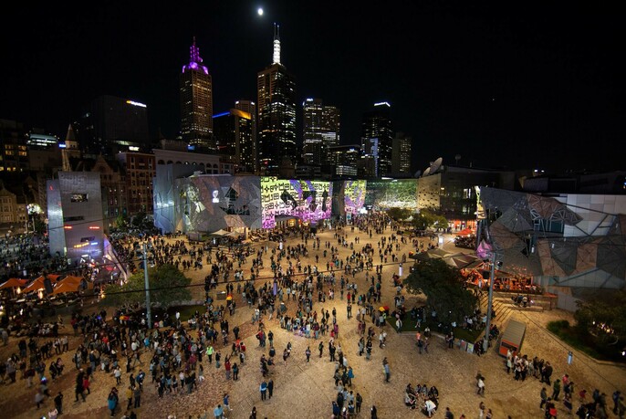 Large crowd in Federation Square at night.