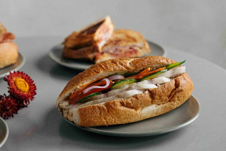 A long roll stuffed with salad ingredients and a toasted sandwich in the background. 