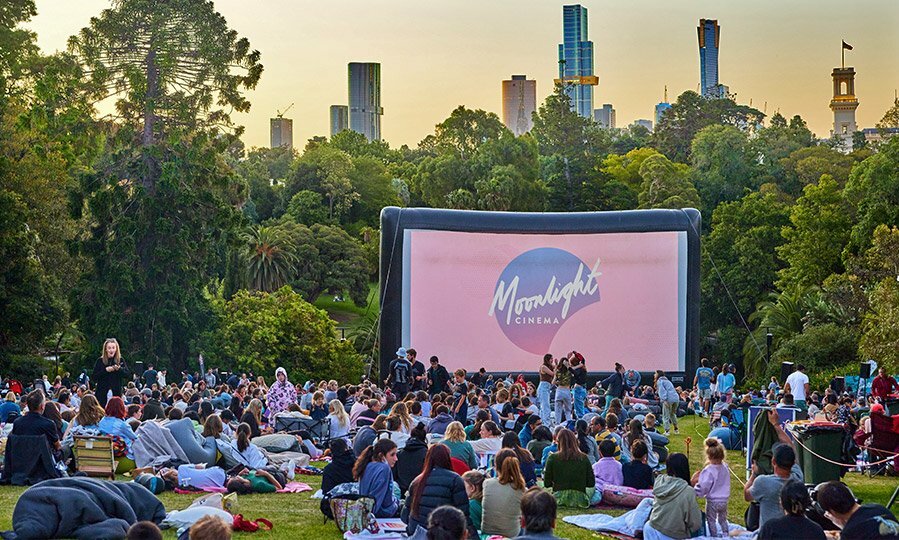 Crowd of people seated on the grass watching Moonlight Cinema in the Royal Botanic Gardens.