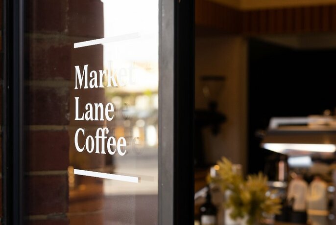 Signage on a shop  window that says 'Market Lane Coffee' with glimpses of coffee making equipment in the background.