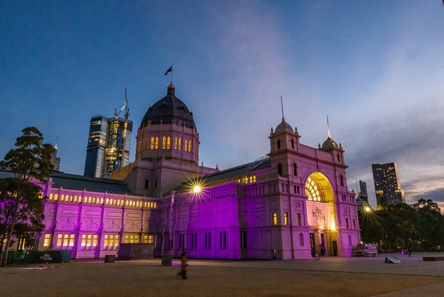 World Heritage listed Royal Exhibition Building illuminated with a purple light at dusk.