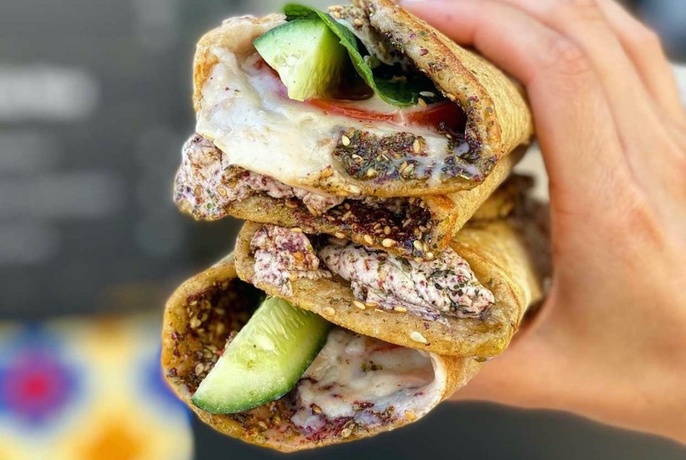 Hand holding Lebanese flatbread sandwiches with cucumber, sauce and other fillings.