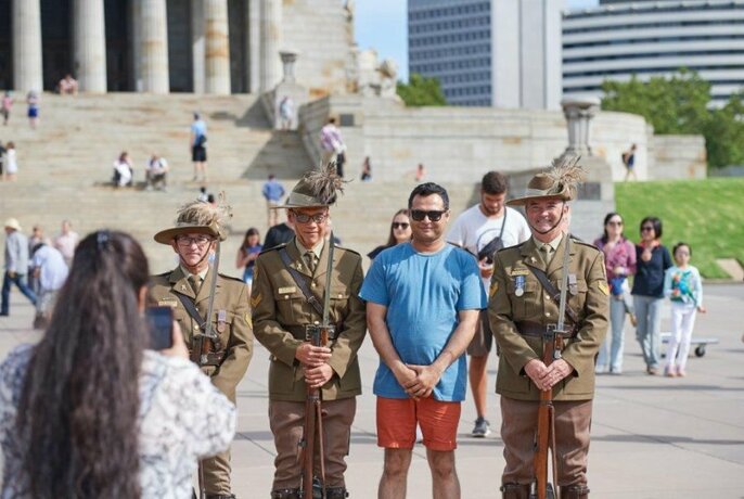 Woman taking a photograph of a man standing between solders outside the Shrine of Remembrance.
