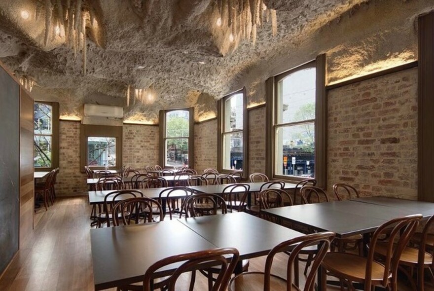 Empty restaurant interior with stalactite-decorated ceiling, brick walls and rows of tables and chairs.