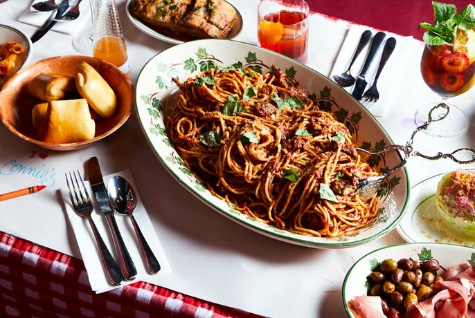 A table with a plate of spaghetti and rolls and olives on the side. 