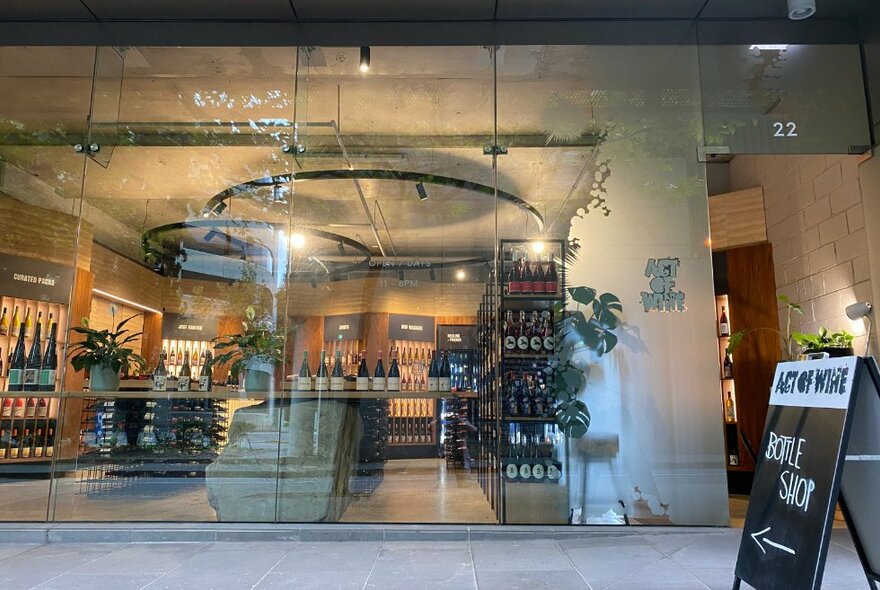 The shopfront of a wine store, looking in through floor-to-ceiling panes of glass at the wooden wine shelves within.