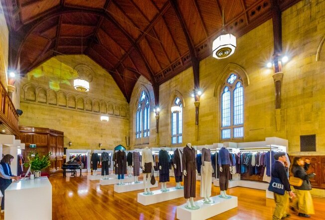 Mannequins and shelves displaying clothing in a fashion store located in an old building with a high ceiling and arch windows