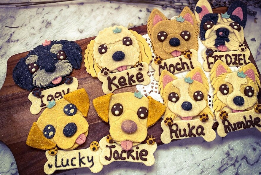 Decorated dog-shaped cookies with names iced on bone-shaped cookies, on a marble surface.