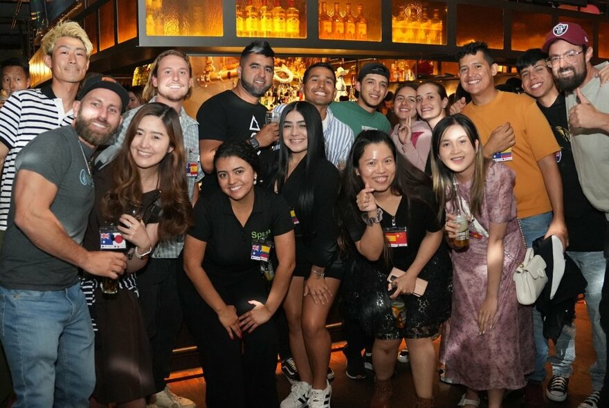 Large group of people smiling in front of a bar in a pub.