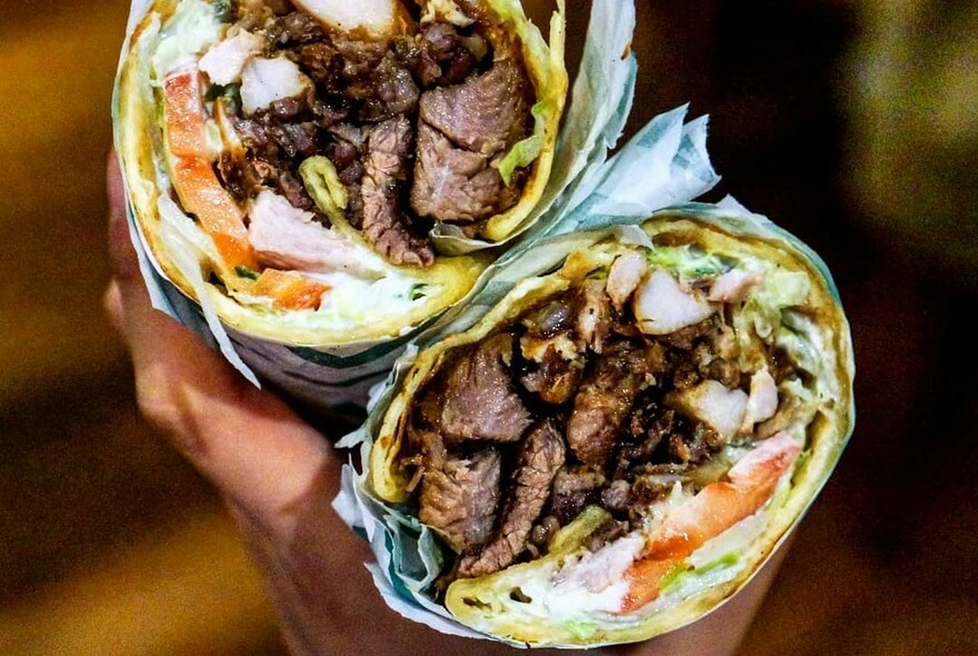Hand holding a halved souvlaki in paper wrapping.