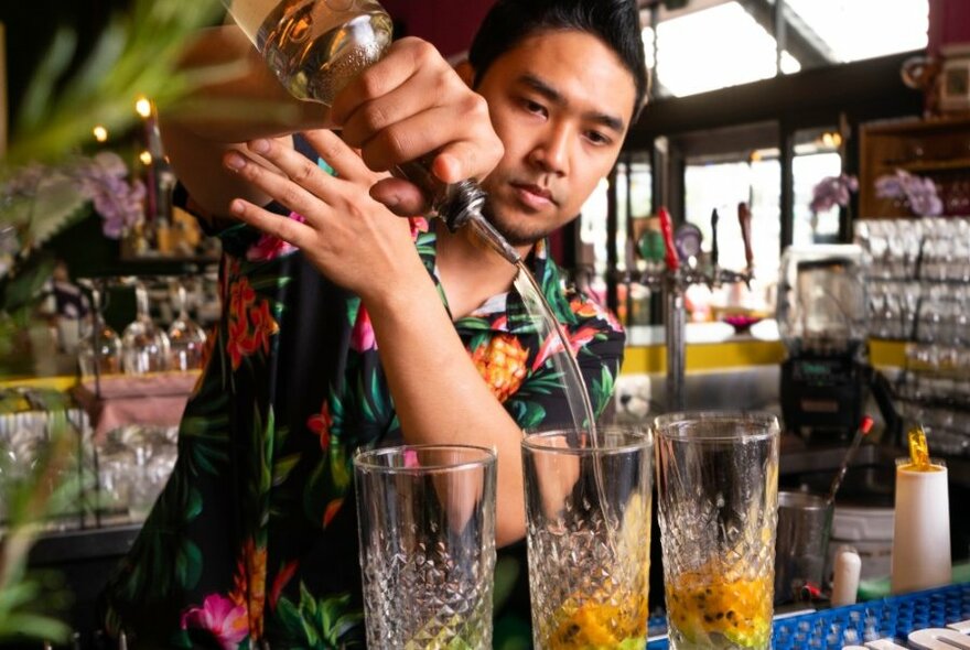 A bartender in a Hawaiian shirt pouring cocktails with passionfruit. 