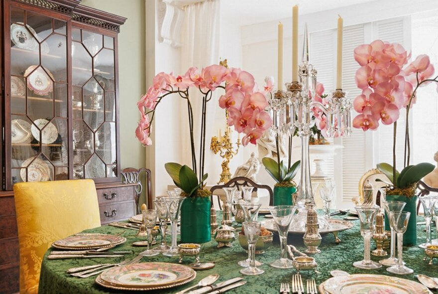 A Georgian dining room with a table set for dinner and vases of pink orchids and candelabras on the table. 