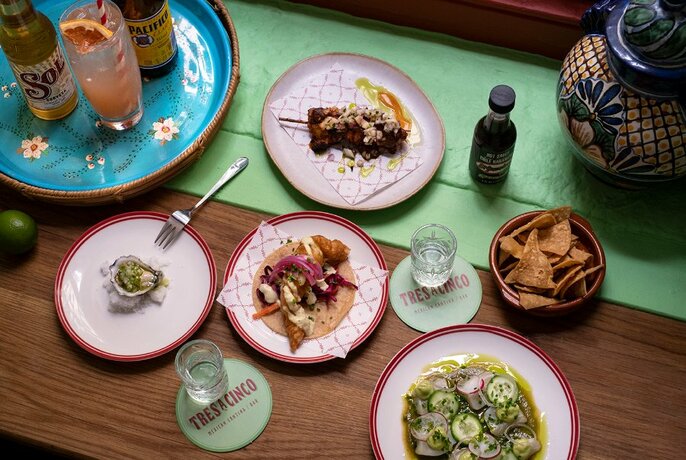 Table covered with tacos, seafood dishes, corn chips and Mexican beers.