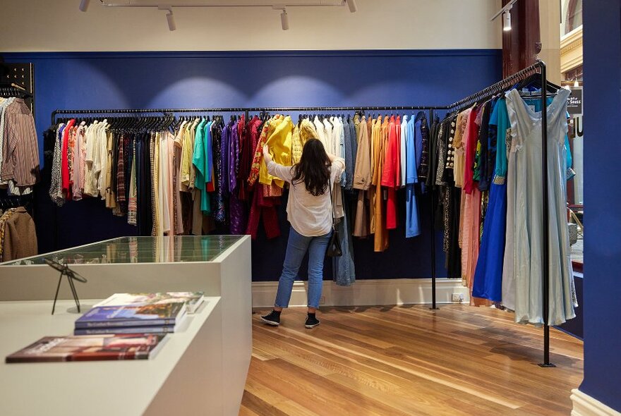 A woman browsing colour-coordinated clothing racks in a vintage fashion boutique.