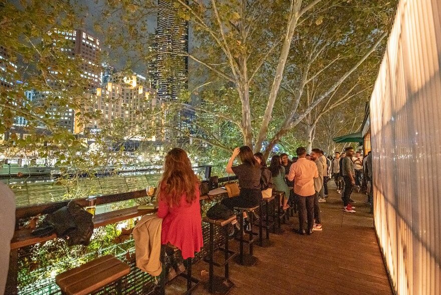 People sitting at an outdoor bar, overlooking the Yarra River. 