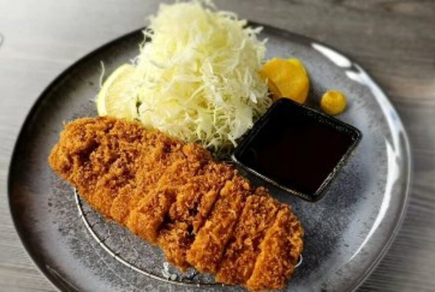 Tonkatsu, Japanese crumbed pork fillet, with shredded daikon and dipping sauce on a grey serving plate.