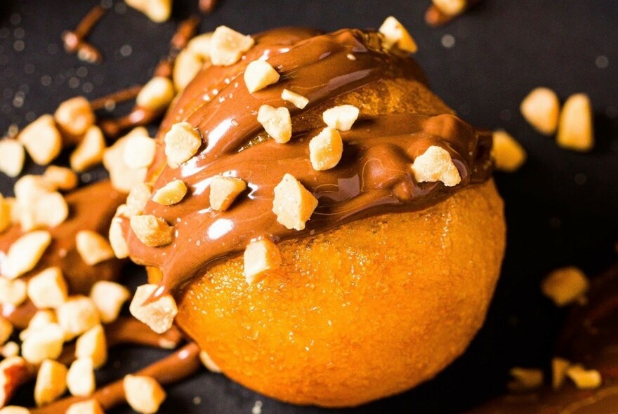 A lukumade ball with chocolate sauce and nuts.