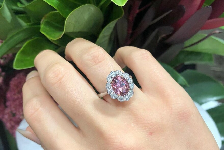 Model's hand with a ring, with a pink stone surrounded by diamonds.