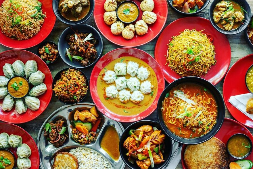 Overhead view of many varied dishes of Nepalese food on a table including soup, noodles and dumplings.