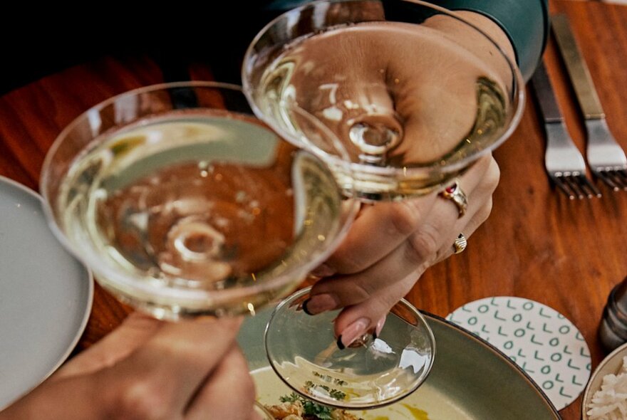 Two champagne glasses being clinked by two hands over a table.