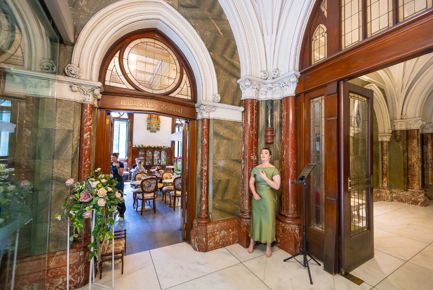 A woman in a corner in a very grand and formal-looking  period building.