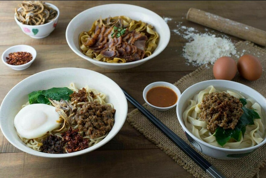 A selection of noodle dishes with eggs, flour and a rolling pin in the background. 