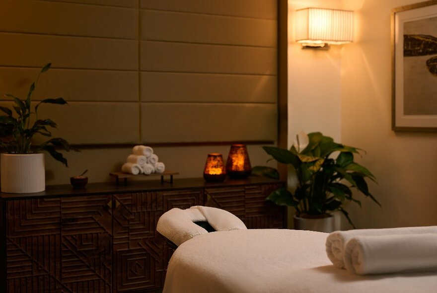 A spa room with white towels and table, candles and dim lighting.
