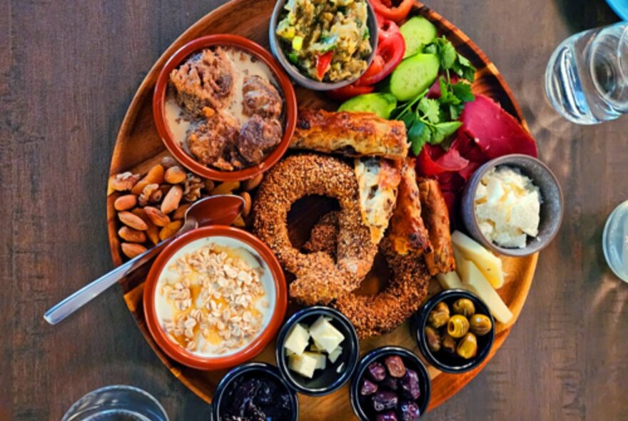 A round tray filled with Turkish snacks including bowls of dips, olives and salads.