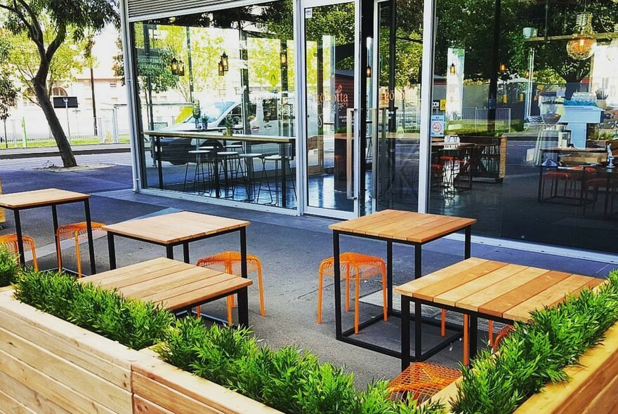Exterior of cafe with tables and orange stools, looking across to large glass windows of the cafe interior.