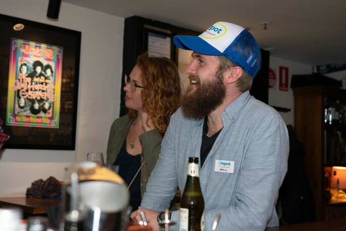 Man with a cap laughing in a bar with a woman beside him. 