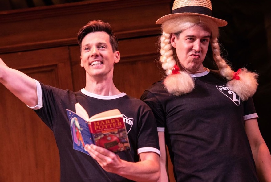 Two actors onstage, one wearing a blonde wig with pigtails and the other reading aloud from a Harry Potter book.